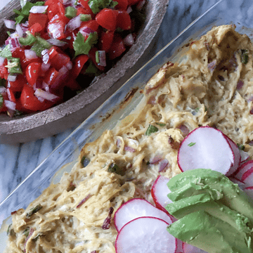 Green chili enchilada casserole in a pan with raddish and avocado on top with pico de gallo on the side