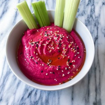 Cauliflower beat hummus with celery in a white bowl