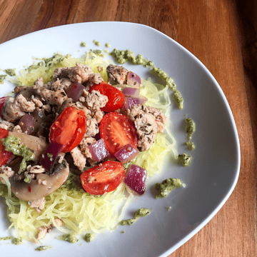 fresh pesto spaghetti squash on at plate with tomatoes and ground meat.