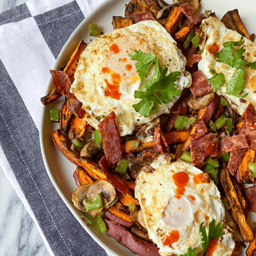 Loaded Breakfast fries on a plate with sweet potatoes, veggies, eggs, and bacon