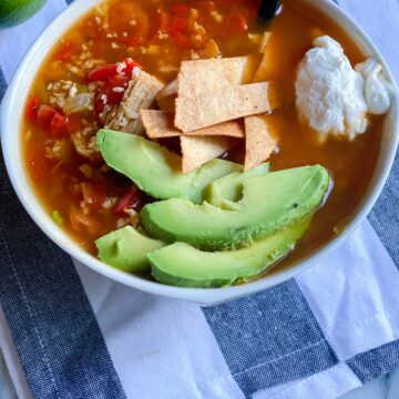 Paleo Chicken Tortilla Soup in a bowl topped with avocado, sour cream and grain free tortillas