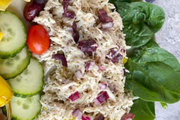 Greek inspired chicken salad on a plate with spinach, tomatoes, cucumbers and carrots