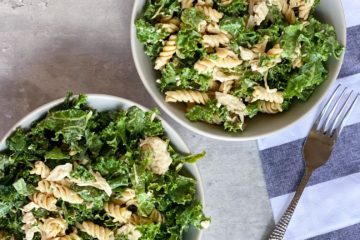 kale caesar pasta salad in two bowls with a fork