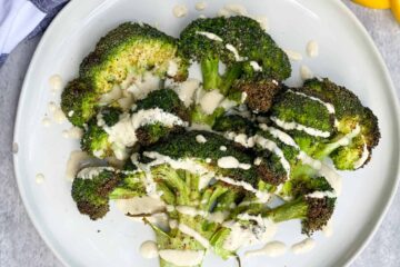 Crispy Broccoli with lemon tahini sauce drizzled over the top on a white plate