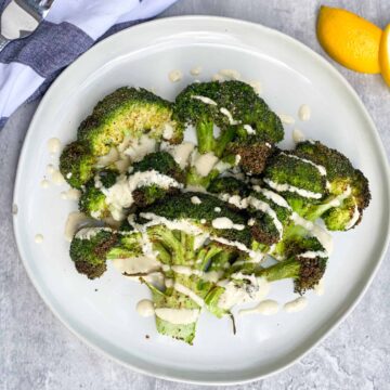 Crispy Broccoli with lemon tahini sauce drizzled over the top on a white plate