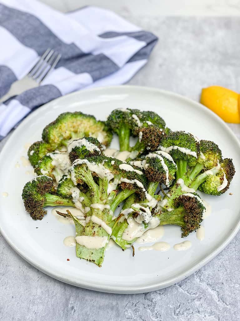 Crispy Broccoli with lemon tahini sauce drizzled over the top on a white plate