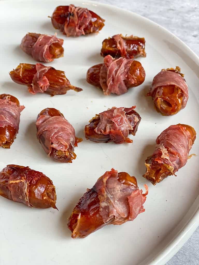 Prosciutto wrapped dates on a white plate