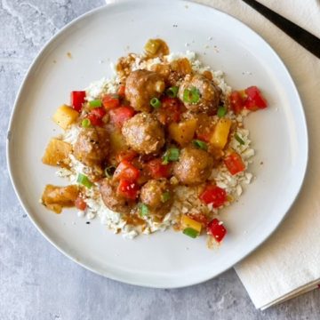 Sweet and Sour Meatballs on a plate with red peppers, pineapple chunks and green onions